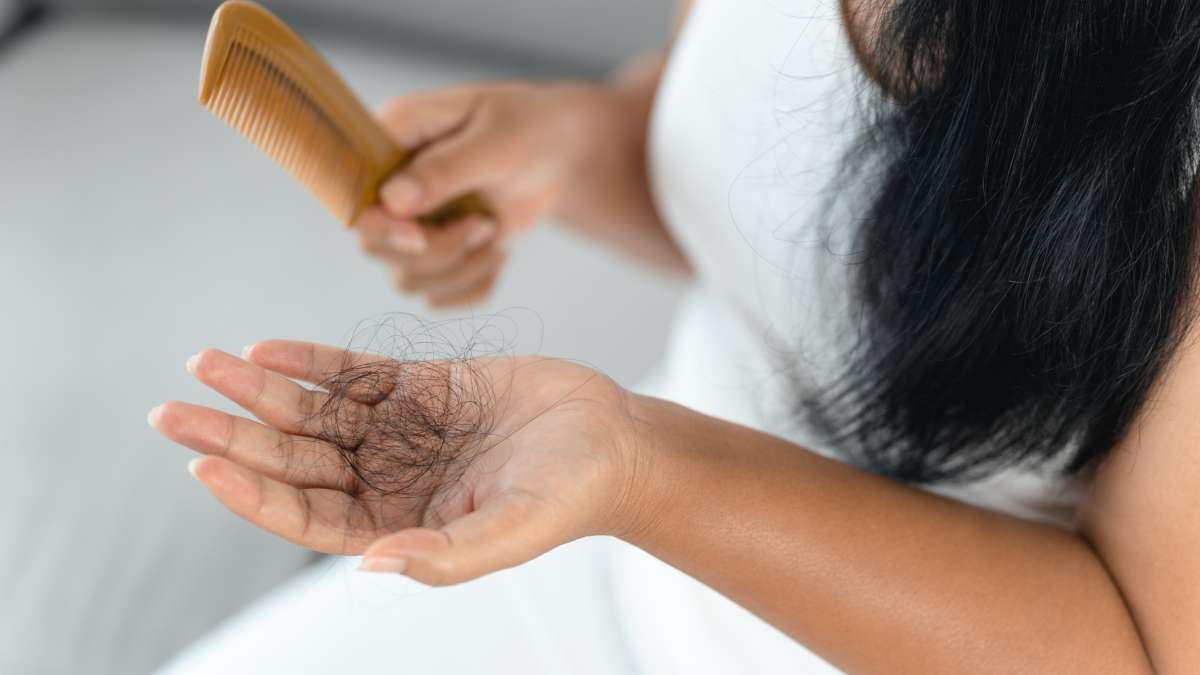 Frau hält eine Haarbürste und eine Handvoll ausgefallener Haare in der Hand